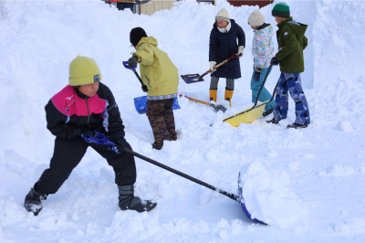 雪を片付ける1年生と担任教師